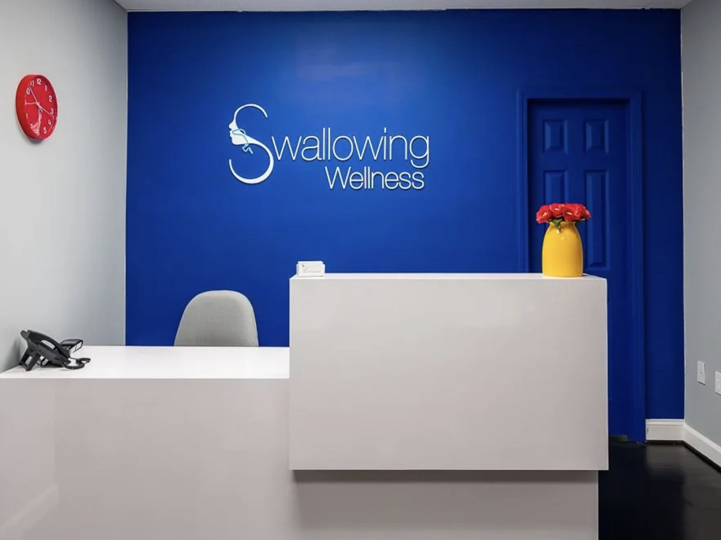 The Swallowing Wellness reception — a bright front desk in front of the practice's blue logo wall